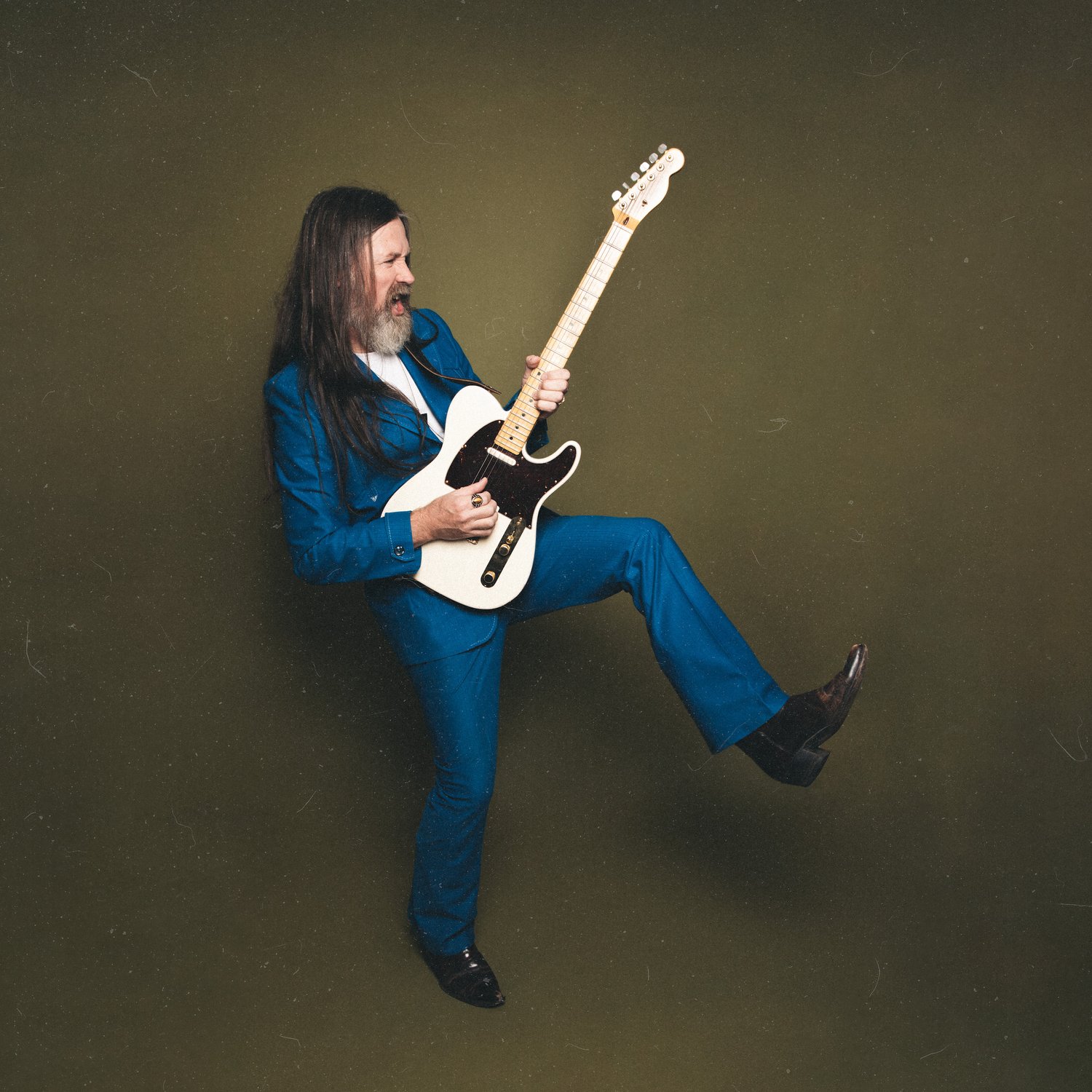 Leroy Powell in a blue suit playing a white electric guitar against an olive studio backdrop