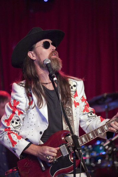 Leroy Powell singing and playing a red electric guitar in a white skull-patterned stage jacket