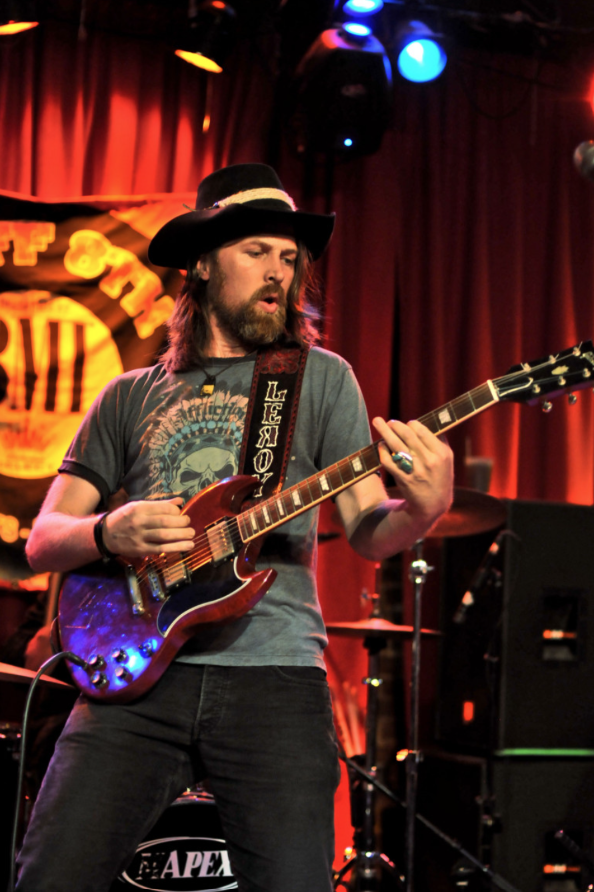 Leroy Powell performing with a red electric guitar in front of a red stage curtain