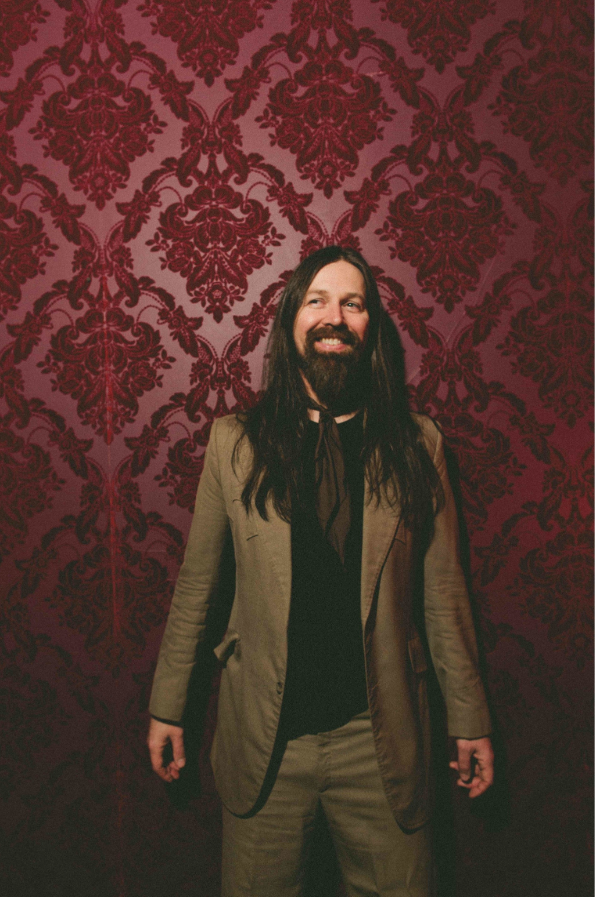Portrait of Leroy Powell standing in front of patterned red wallpaper