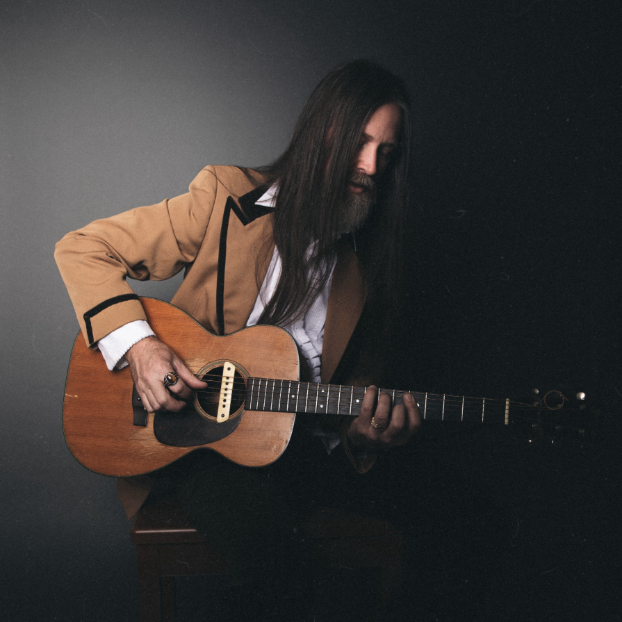 Leroy Powell playing an acoustic guitar in a tan western jacket