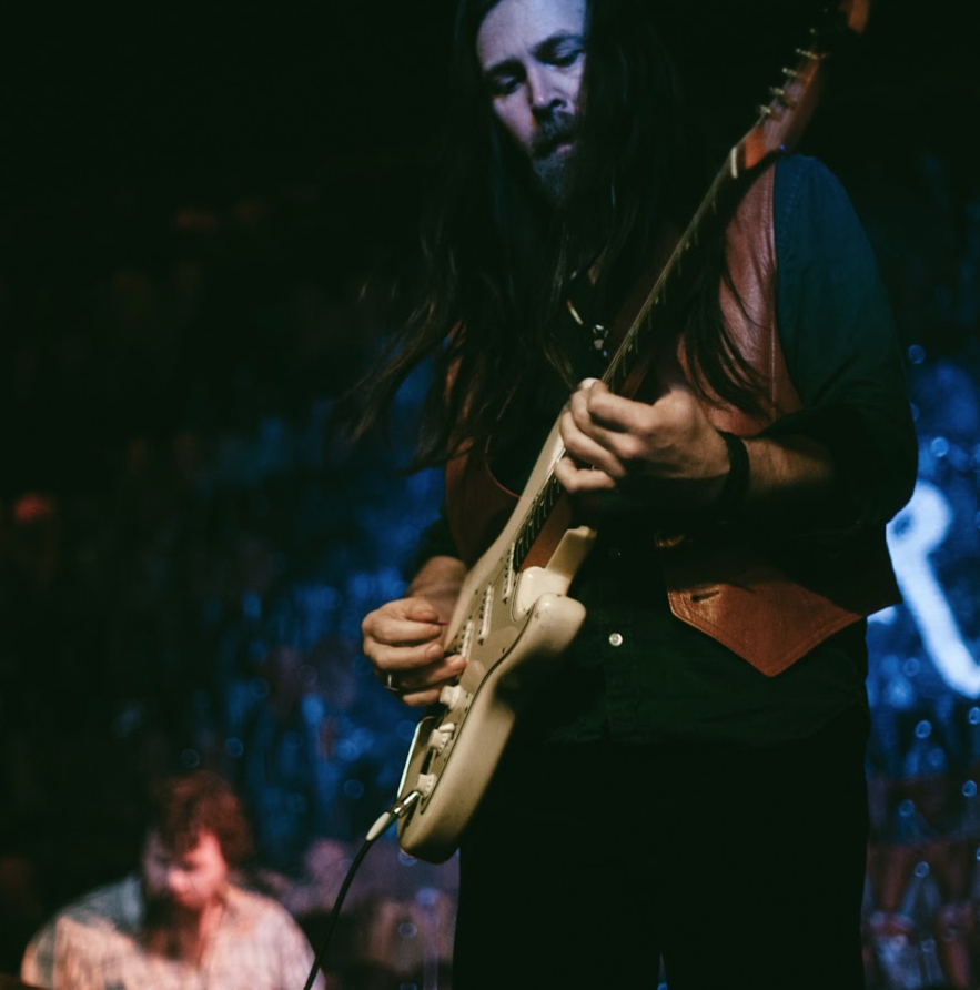 Leroy Powell playing a white electric guitar under blue stage light
