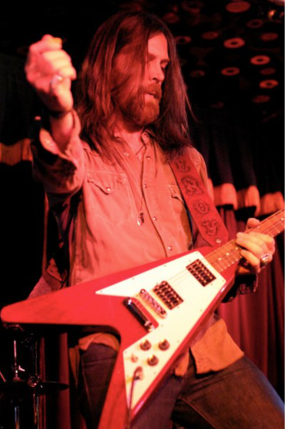 Leroy Powell performing onstage under red light with a red Flying V guitar