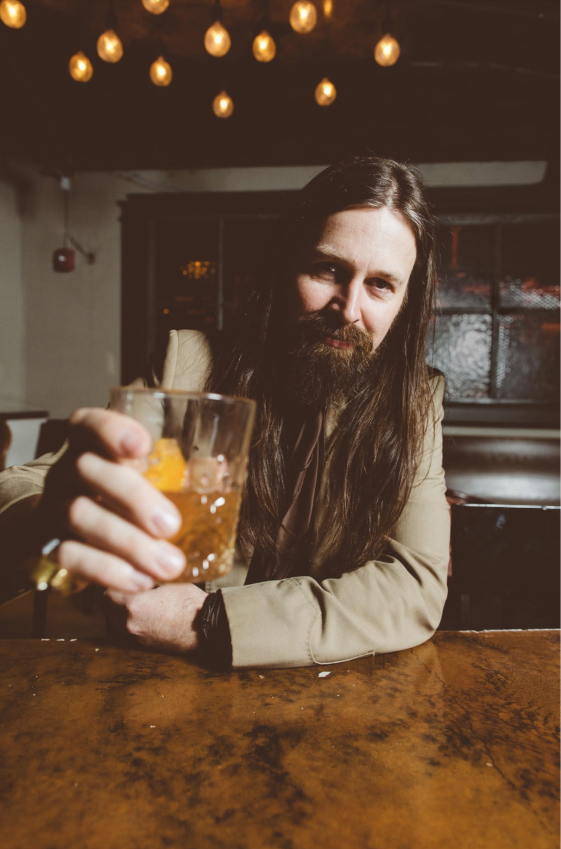 Leroy Powell raising a glass at a bar beneath warm hanging lights
